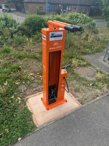 An orange bike repair station in the ground with a stand a pump