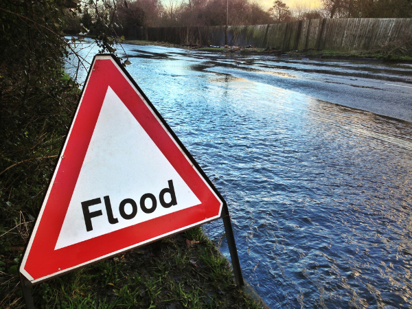 Road sign with flood warning and flooded road in the background